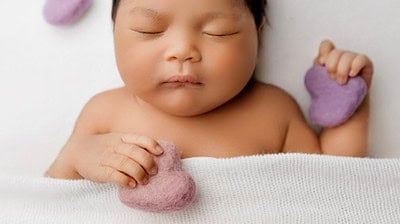 Adorable sleeping baby with heart-shaped felted pillows, perfect for newborn and baby photography.